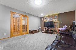 Living area featuring light grey carpeting, a brick-faced fireplace, a brown accent wall, and a textured ceiling - 