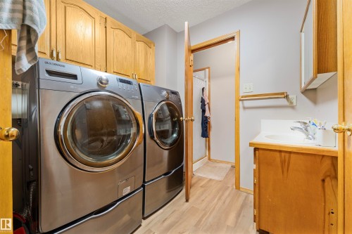 Laundry area featuring wood-finish flooring and upper cabinetry - 4231 32 Avenue, Edmonton, AB - Indoor Photo Showing Laundry Room