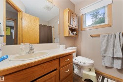 Bathroom featuring a wood vanity with a white countertop and oval sink, a wall-mounted mirror, a window with a white blind, and light wood trim - 