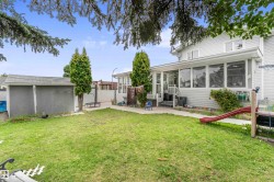 Expansive grassy yard area featuring a detached shed with a shingled roof, mature evergreen trees, and a screened-in porch with an exterior staircase - 