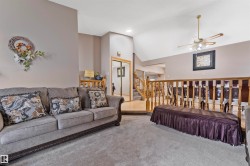 Carpeted living area featuring vaulted ceilings, a ceiling fan with integrated lighting, and a wood baluster railing - 