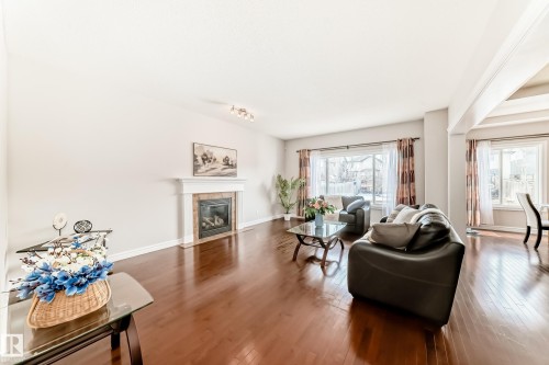 Spacious living area featuring rich wood-finish flooring, a white mantel fireplace, and large windows with natural light - 1330 114B Street, Edmonton, AB - Indoor Photo Showing Living Room With Fireplace