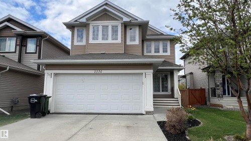 Two-story residence featuring light brown and dark brown siding, an attached two-car garage, multiple upper-level windows, a front entry with steps, and a landscaped front yard with a tree - 1330 114B Street, Edmonton, AB - Outdoor With Facade