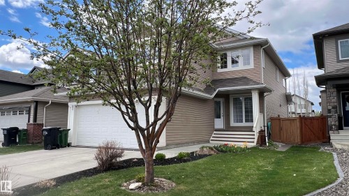 Two-story residential exterior featuring tan siding, a front entry with white steps, a covered porch, and a two-car garage - 1330 114B Street, Edmonton, AB - Outdoor