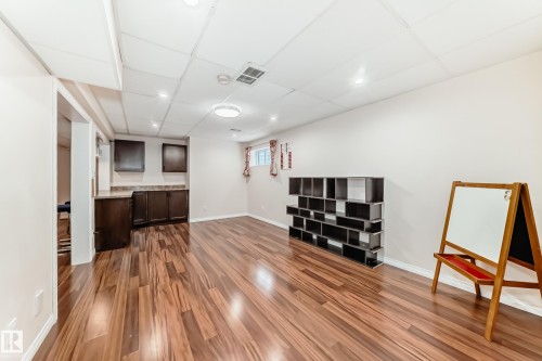 Spacious finished room featuring wood-finish flooring, recessed lighting, and a built-in wet bar with dark cabinetry and a stone-look countertop - 1330 114B Street, Edmonton, AB - Indoor