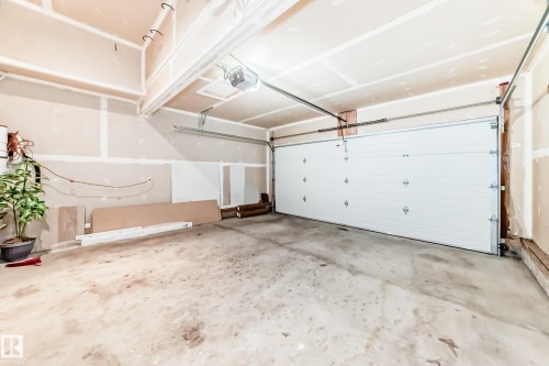 Spacious garage featuring a white panel garage door, unfinished drywall, exposed ceiling joists, and a concrete floor - 1330 114B Street, Edmonton, AB - Indoor Photo Showing Garage
