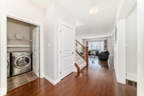 Hallway featuring wood-finish flooring, a laundry closet with tile flooring and wire shelving, and a carpeted staircase with wood banister - 1330 114B Street, Edmonton, AB - Indoor Photo Showing Laundry Room
