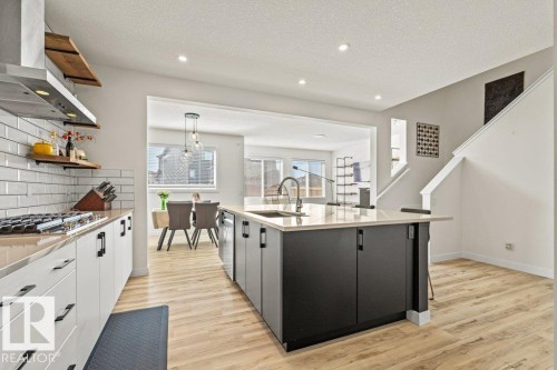 Modern kitchen featuring a large central island with seating, light wood-finish flooring, white subway tile backsplash, stainless steel appliances, and recessed lighting - 21003 131 Avenue, Edmonton, AB 