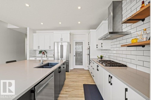Contemporary kitchen featuring a large central island with an undermount sink, stainless steel appliances, white subway tile backsplash, and wood-finish flooring - 21003 131 Avenue, Edmonton, AB 