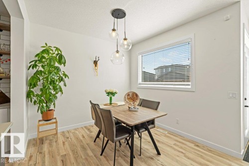 Dining area featuring wood-finish flooring, a contemporary pendant light fixture, and a large window with blinds - 21003 131 Avenue, Edmonton, AB 