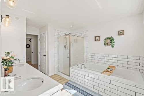 Bathroom featuring a double vanity with undermount sinks, a freestanding bathtub with subway tile surround, a glass-enclosed shower, and wood-finish flooring - 21003 131 Avenue, Edmonton, AB 