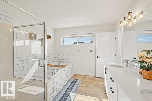 Contemporary bathroom featuring a glass-enclosed shower, white subway tile accents, wood-finish flooring, a double vanity with undermount sinks, and a large soaking tub - 21003 131 Avenue, Edmonton, AB 