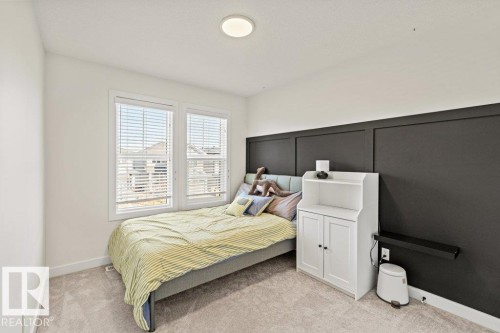 White walls complementing a dark accent wall with panel detailing, light-colored carpet, two windows with blinds, and a flush-mount ceiling light - 21003 131 Avenue, Edmonton, AB 