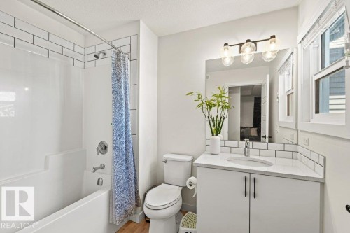 Bathroom featuring a combination bathtub and shower, white subway tile surround, white vanity with integrated sink, stone countertop, and wood-finish flooring - 21003 131 Avenue, Edmonton, AB 
