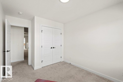 Interior room featuring light gray carpet, white walls, and a built-in closet with panel doors and black hardware - 21003 131 Avenue, Edmonton, AB 