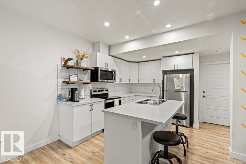 Kitchen featuring white cabinetry, stainless steel appliances, a subway tile backsplash, recessed lighting, and wood-finish flooring - 21003 131 Avenue, Edmonton, AB 
