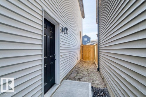 Side entry with a black paneled door, exterior wall lantern, and concrete landing - 21003 131 Avenue, Edmonton, AB 