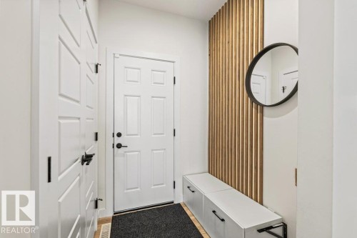 Entryway featuring a white paneled door with matte black hardware, wood slat accent wall, and built-in storage bench - 21003 131 Avenue, Edmonton, AB 