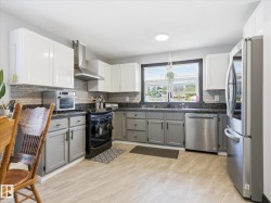 Kitchen featuring light wood-finish flooring, two-tone cabinetry with white upper and gray lower cabinets, a mosaic tile backsplash, and dark countertops - 