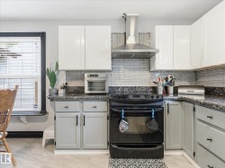Kitchen featuring a black electric range, stainless steel range hood, and light gray cabinetry with black hardware - 
