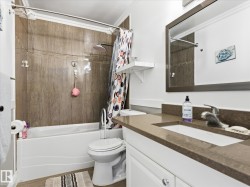 Bathroom featuring a tub/shower combination with stone-finish tile surround, a built-in shelf, and a ceiling-mounted showerhead - 