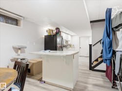 Lower-level living area featuring wood-finish flooring, a white kitchen with cabinetry, and a kitchen island with a light-toned countertop - 