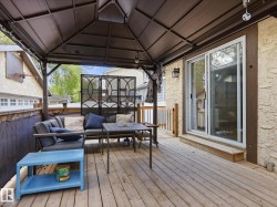Expansive wood-plank deck featuring a covered gazebo structure, stucco exterior, privacy screen, and a sliding glass door for interior access - 