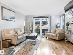 Living area featuring wood-finish flooring, light-toned wall paint, white crown molding, and a large sliding glass door leading to an outdoor space - 