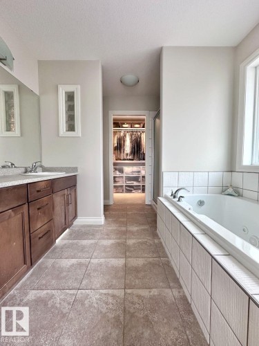 Spacious bathroom featuring a dual vanity with wood-finish cabinetry, a large jetted tub with tile surround, and a walk-in closet with built-in organization - 820 Drysdale Run, Edmonton, AB - Indoor Photo Showing Bathroom