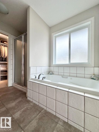 Soaking tub with a tiled surround, frosted window, and chrome fixtures - 820 Drysdale Run, Edmonton, AB - Indoor Photo Showing Bathroom