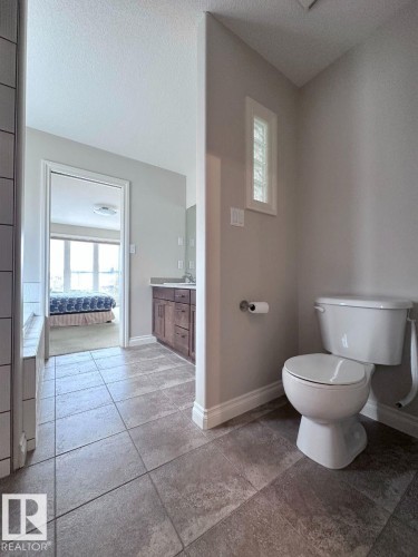 Bathroom featuring large format floor tiling, a white toilet, and a glass block privacy window - 820 Drysdale Run, Edmonton, AB - Indoor Photo Showing Bathroom