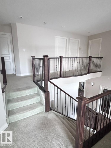 Upper-level landing featuring light-toned carpeting, dark wood-finish newel posts, and wrought iron balusters - 820 Drysdale Run, Edmonton, AB - Indoor Photo Showing Other Room