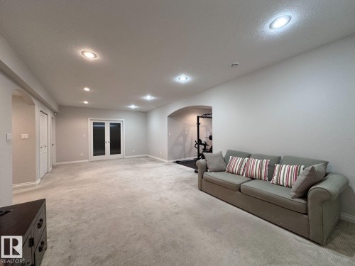 Spacious room featuring light gray carpeting, recessed ceiling lighting, a curved archway, and double French doors with frosted glass panels - 820 Drysdale Run, Edmonton, AB - Indoor