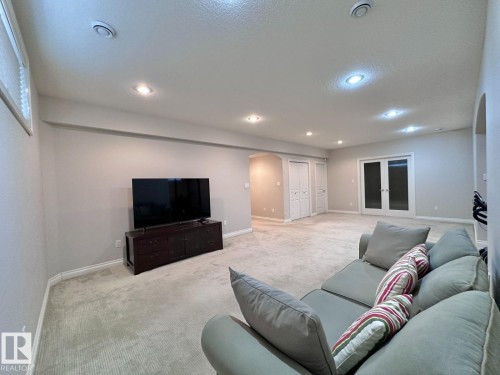 Spacious room featuring neutral carpeting, recessed lighting, white baseboards, and double French doors with frosted glass - 820 Drysdale Run, Edmonton, AB - Indoor