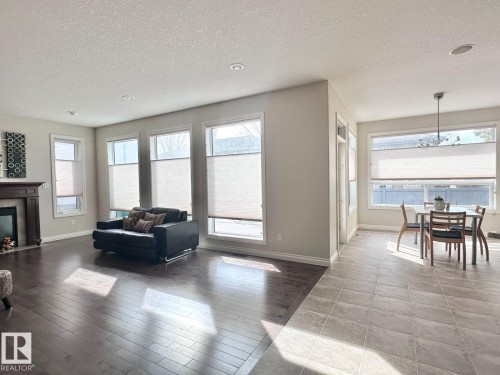Open-concept living space featuring rich wood-finish flooring, a fireplace with a wood mantle, numerous windows with blinds, and recessed lighting - 820 Drysdale Run, Edmonton, AB - Indoor Photo Showing Living Room With Fireplace