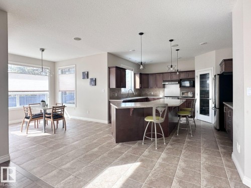 Spacious kitchen featuring an L-shaped island with seating, dark wood cabinetry, stainless steel appliances, and tile flooring - 820 Drysdale Run, Edmonton, AB - Indoor