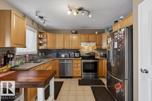 The kitchen features light wood cabinetry, stainless steel appliances, a tile backsplash, and track lighting - 16107 92 Street, Edmonton, AB - Indoor Photo Showing Kitchen With Stainless Steel Kitchen With Double Sink