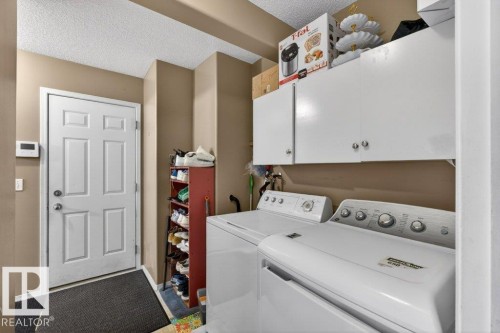 This utility area features a white paneled door, a washer and dryer, and white overhead cabinetry for storage - 16107 92 Street, Edmonton, AB - Indoor Photo Showing Laundry Room