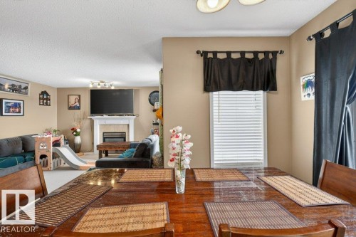 Dining area with a window providing natural light, leading into a living space featuring a fireplace with a mantel, and a mounted television - 16107 92 Street, Edmonton, AB - Indoor With Fireplace