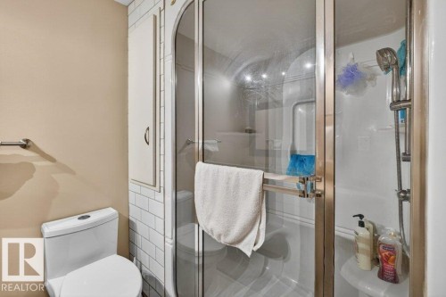Bathroom featuring a white toilet, a built-in storage cabinet with white subway tile surround, and a glass-enclosed shower with a handheld showerhead - 16107 92 Street, Edmonton, AB - Indoor Photo Showing Bathroom