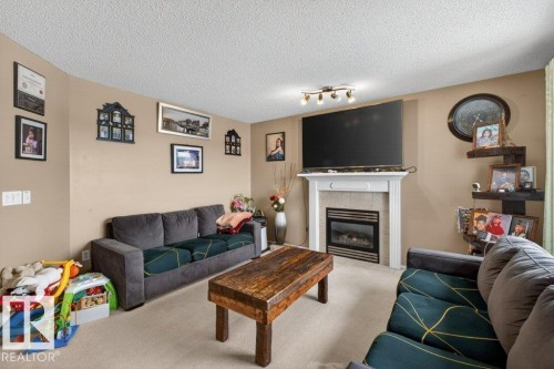 This living area features a fireplace with a white mantel and a light-colored tile surround, set against neutral-toned walls - 16107 92 Street, Edmonton, AB - Indoor Photo Showing Living Room With Fireplace