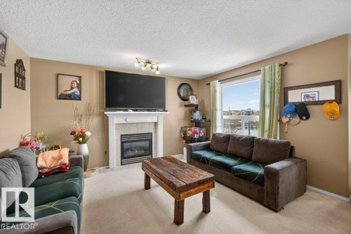 Living area featuring a fireplace with a light-colored mantel, a large window providing natural light, and a textured ceiling - 16107 92 Street, Edmonton, AB - Indoor Photo Showing Living Room With Fireplace