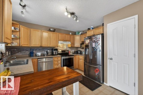 The kitchen features light wood cabinetry, stainless steel appliances, a double basin sink, and a stone-style backsplash - 16107 92 Street, Edmonton, AB - Indoor Photo Showing Kitchen With Stainless Steel Kitchen With Double Sink