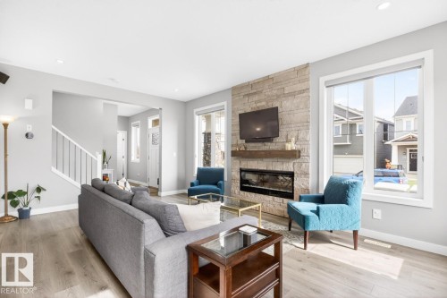 Spacious Living Room with Ample Windows allowing tons of Natural Light, Fireplace, and Open Concept to the Kitchen and Dining Room Space. - 20023 17A Avenue, Edmonton, AB - Indoor Photo Showing Living Room With Fireplace