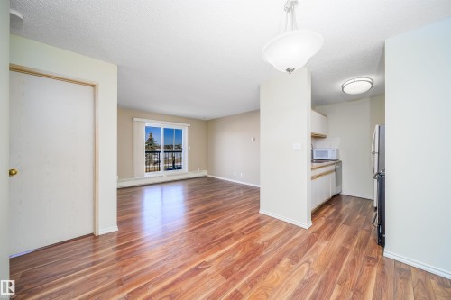 Open-concept living area featuring wood-finish flooring, a sliding glass door with balcony access, and a kitchen alcove with white cabinetry and stainless steel appliances - 213 5065 31 Avenue, Edmonton, AB - Indoor