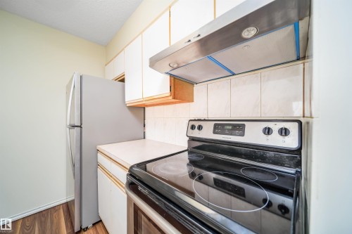 Kitchen featuring a stainless steel range hood, white tile backsplash, and wood-finish flooring - 213 5065 31 Avenue, Edmonton, AB - Indoor Photo Showing Kitchen