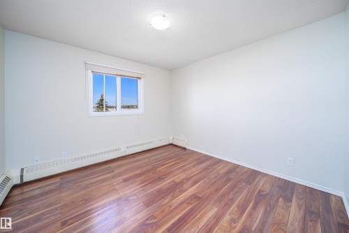Bright room featuring wood-finish flooring, white walls, and a window with a roller blind - 213 5065 31 Avenue, Edmonton, AB - Indoor Photo Showing Other Room