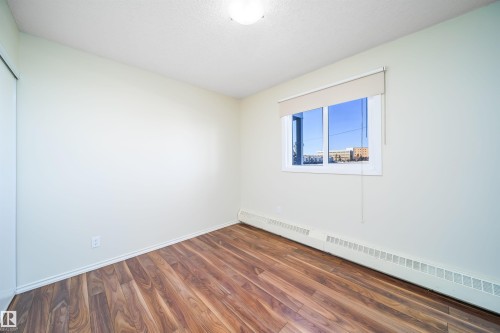Bedroom featuring wood-finish flooring, a window with roller shade, and baseboard heating - 213 5065 31 Avenue, Edmonton, AB - Indoor Photo Showing Other Room