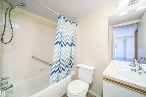Bathroom featuring a tub/shower combination with a grab bar, a white vanity with an integrated sink, a large wall-mounted mirror, and wood-finish flooring - 213 5065 31 Avenue, Edmonton, AB - Indoor Photo Showing Bathroom