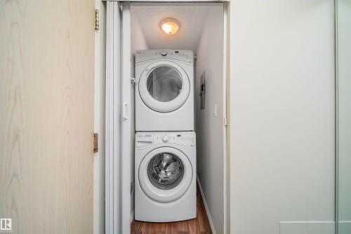 Dedicated laundry closet featuring a stacked white washer and dryer, wood-finish flooring, and overhead lighting - 213 5065 31 Avenue, Edmonton, AB - Indoor Photo Showing Laundry Room